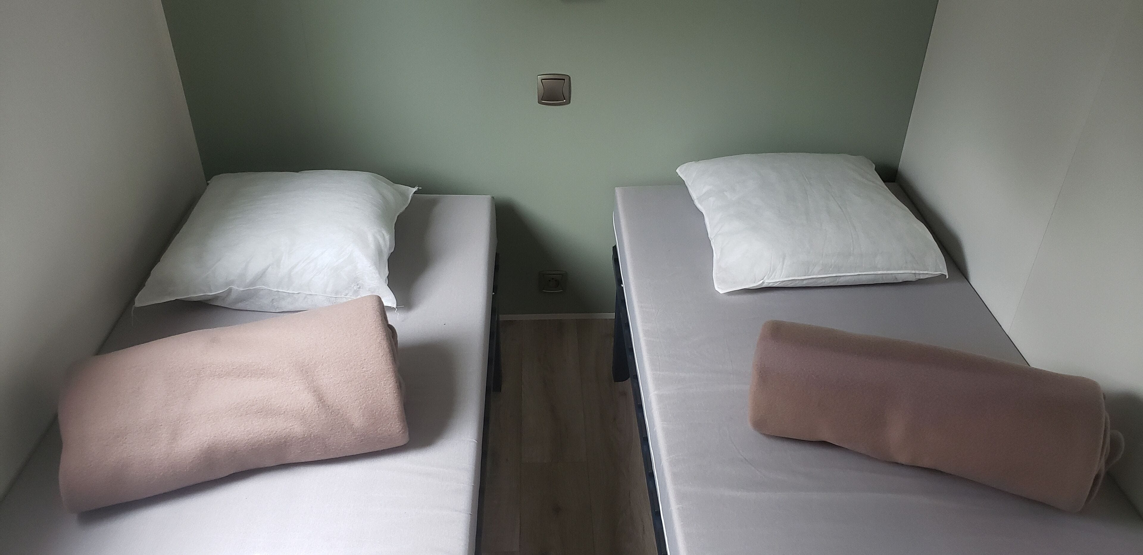 Zwei Einzelbetten mit weißer und rosa Bettwäsche, eine kleine Wandleuchte und Holzboden.