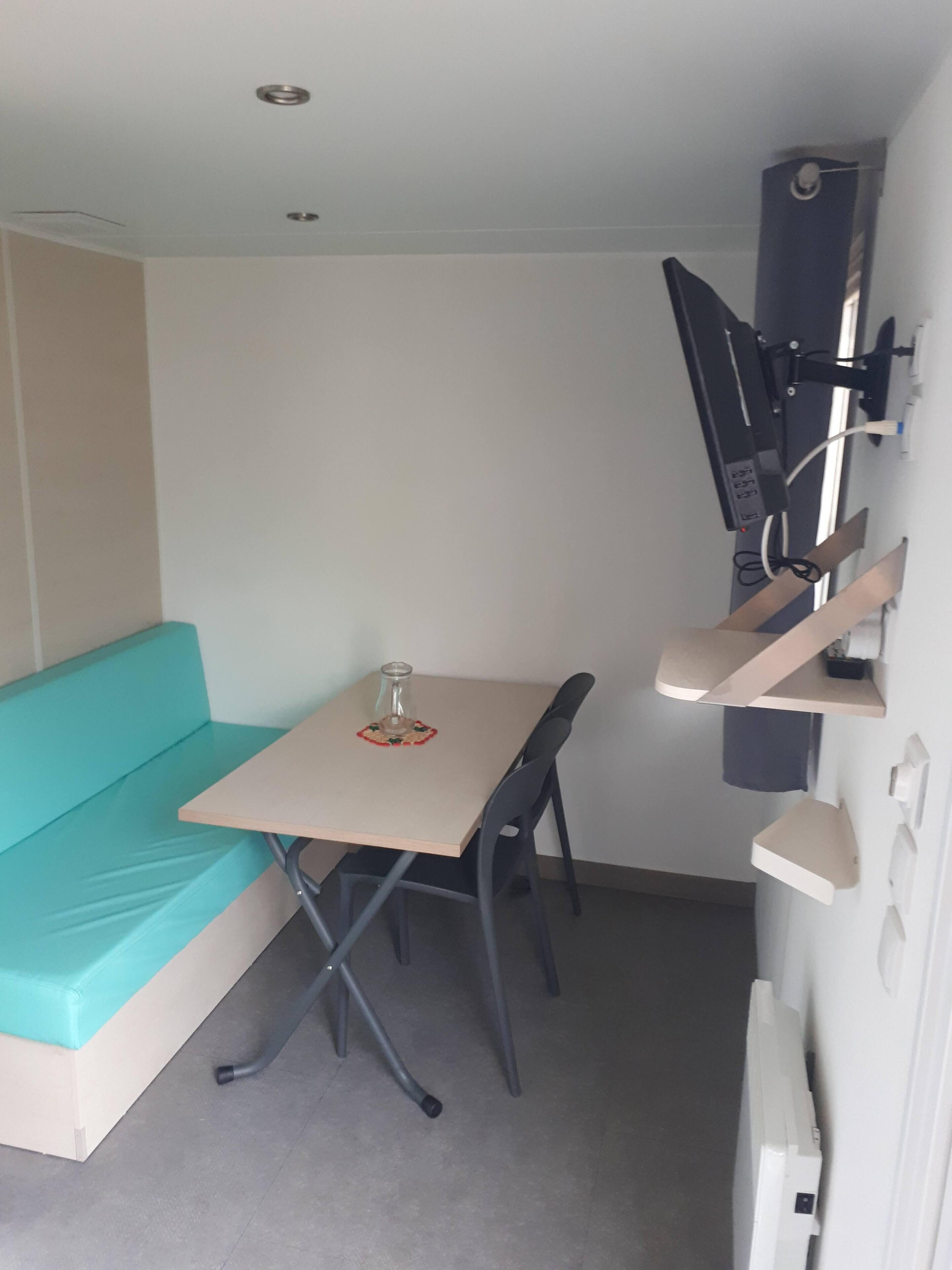 Una habitación compacta con un sofá color turquesa, una mesita con un vaso y un televisor instalado en la pared.