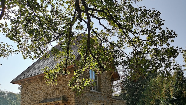 A stone building with a sloped roof, a wooden deck, and a paved entrance area. - Camping Caravaning Des Bondons (La Ferte-sous-Jouarre)