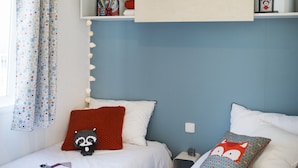 A bedroom with two beds, a shelf above the beds, and a window with curtains. - Camping Caravaning Des Bondons (La Ferte-sous-Jouarre)