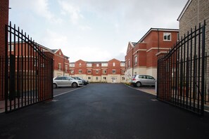 A gated residential area with brick buildings, a paved driveway, and parked cars. - Villetts House (Swindon)