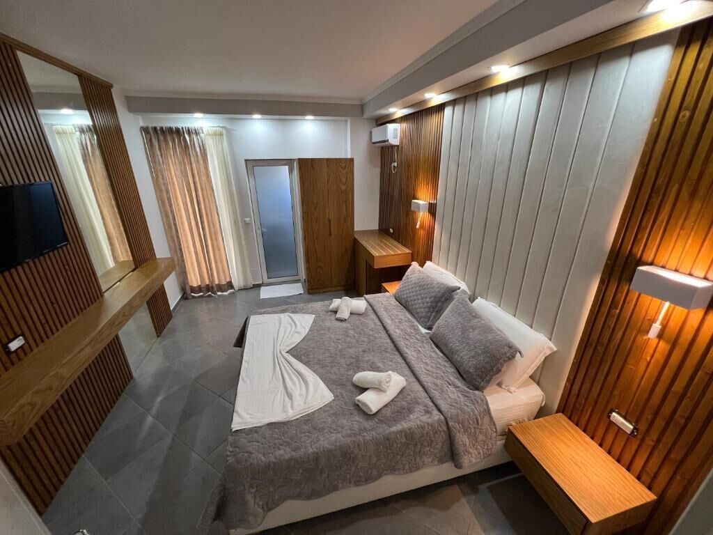 A modern hotel room with a large bed, wooden paneling, a flat-screen TV, and a wooden bench.