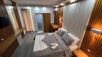 A modern hotel room with a large bed, wooden paneling, a flat-screen TV, and a wooden bench.