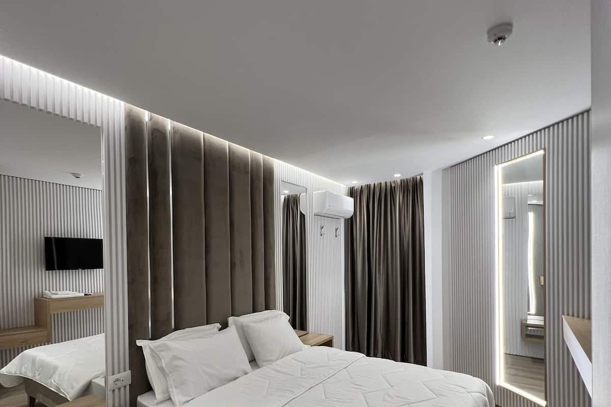 A modern bedroom with a large bed, a wooden bedside table, a built-in TV, and a mirror.