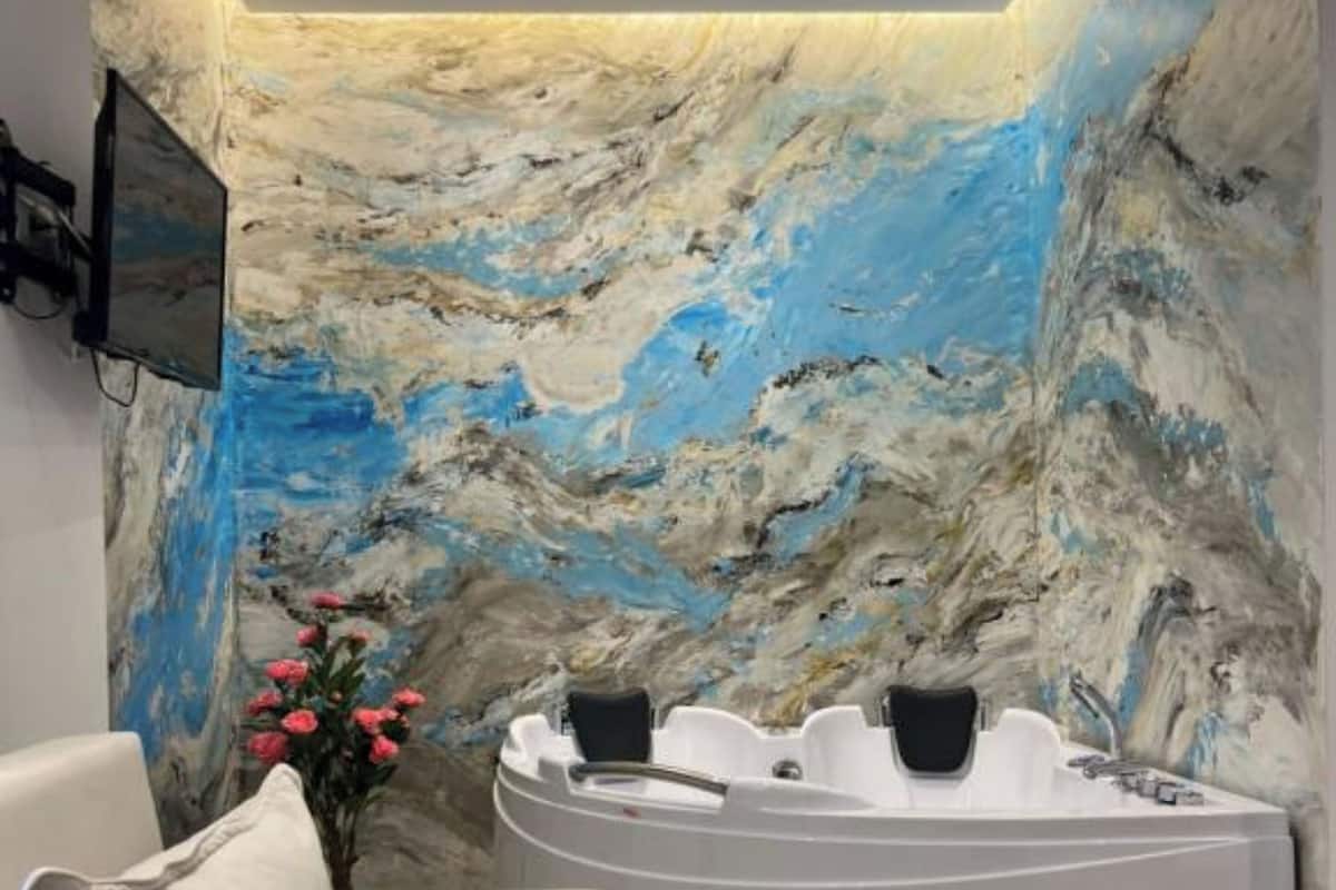 A spa room with a marble wall, a white bathtub, a beige sofa, and a small table with a pink object.