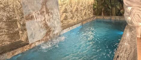 A swimming pool with a waterfall feature, surrounded by a stone wall with carved designs, and a statue on the right.