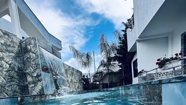 Ein klares Schwimmbecken mit Wasserfall, umgeben von moderner Architektur und tropischer Vegetation.
