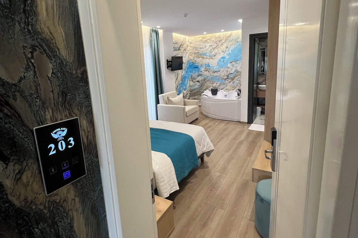 A modern hotel room with a marble wall, a bed with a blue accent, a small seating area, and a bathroom visible through an open door.
