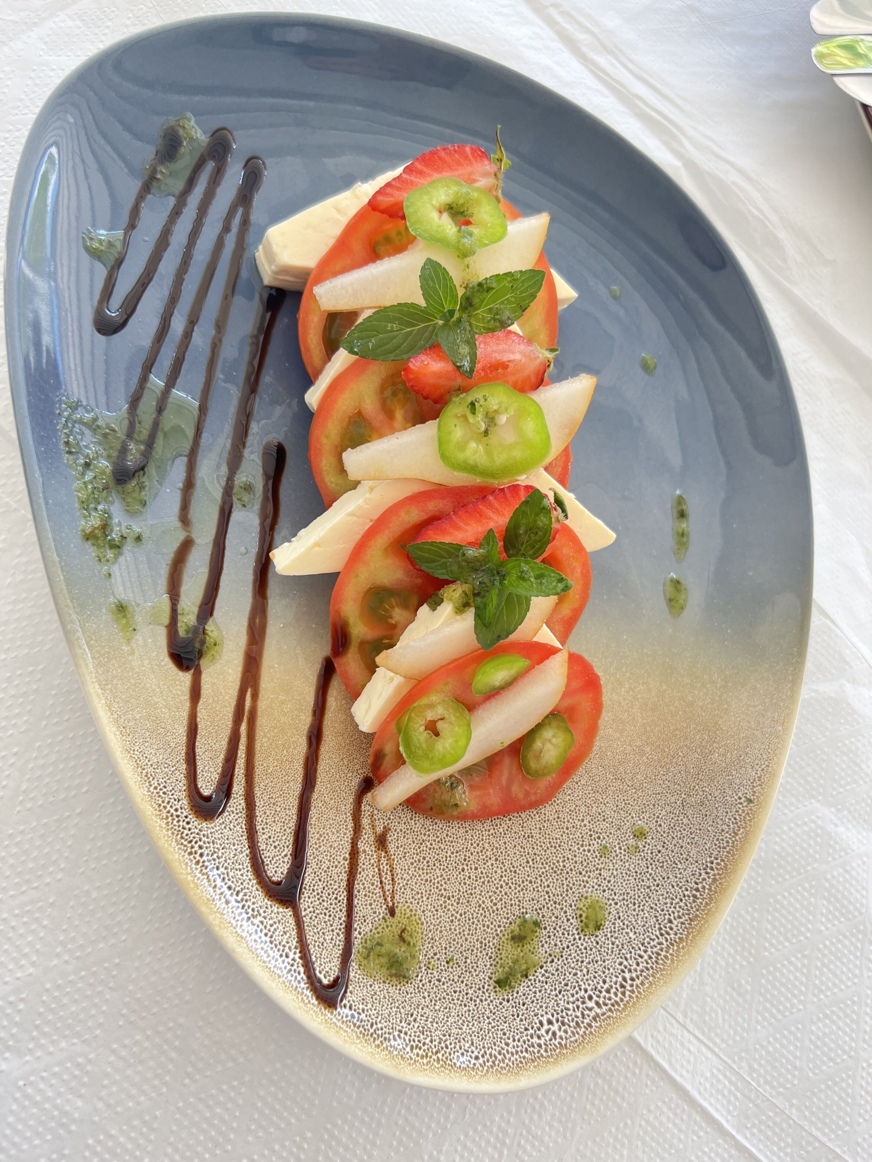 A dessert plate with sliced strawberries, kiwi, mint leaves, and a chocolate drizzle.
