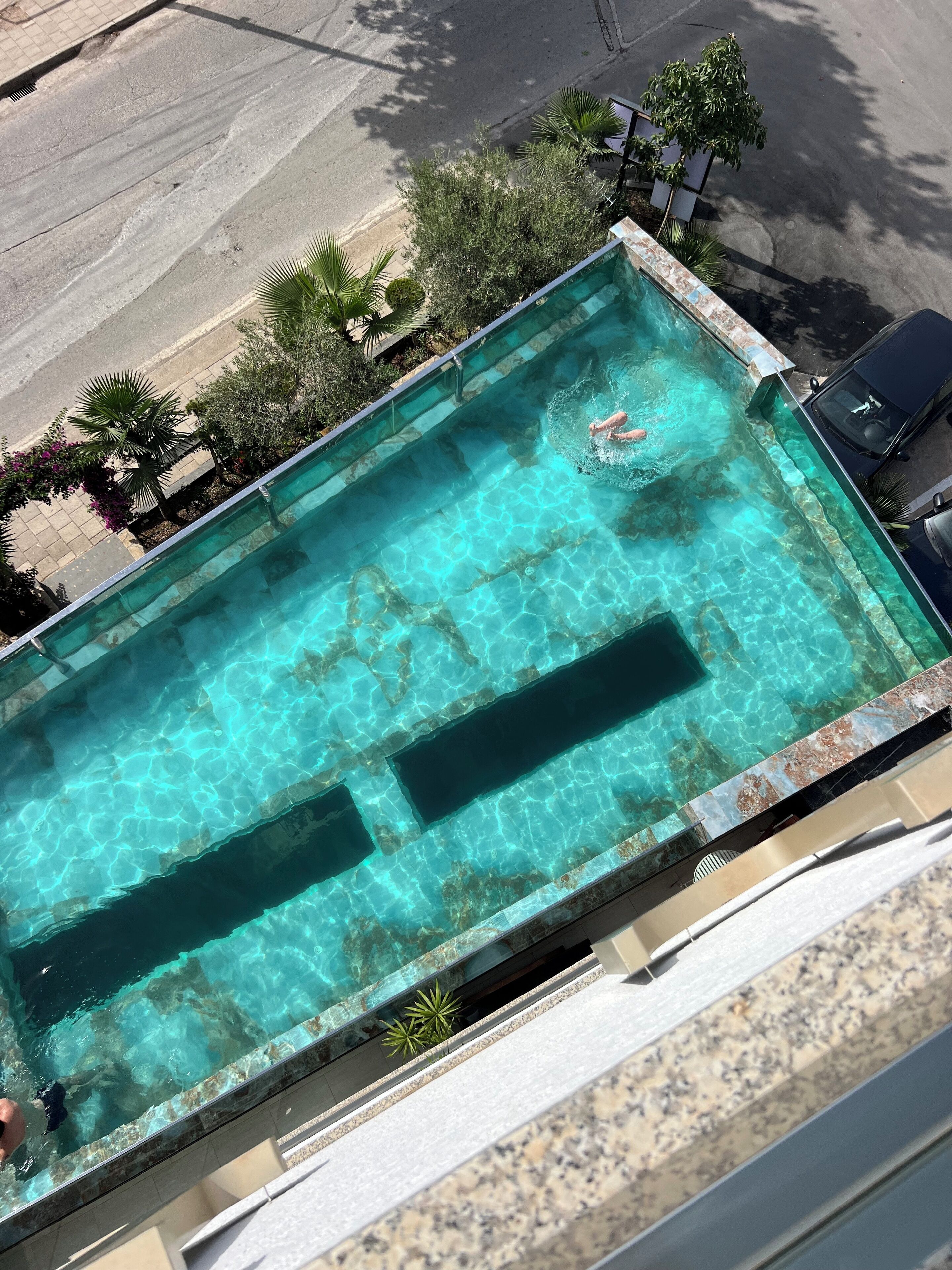 Piscina rectangular con agua cristalina, rodeada de un solado de baldosas y algo de vegetación.