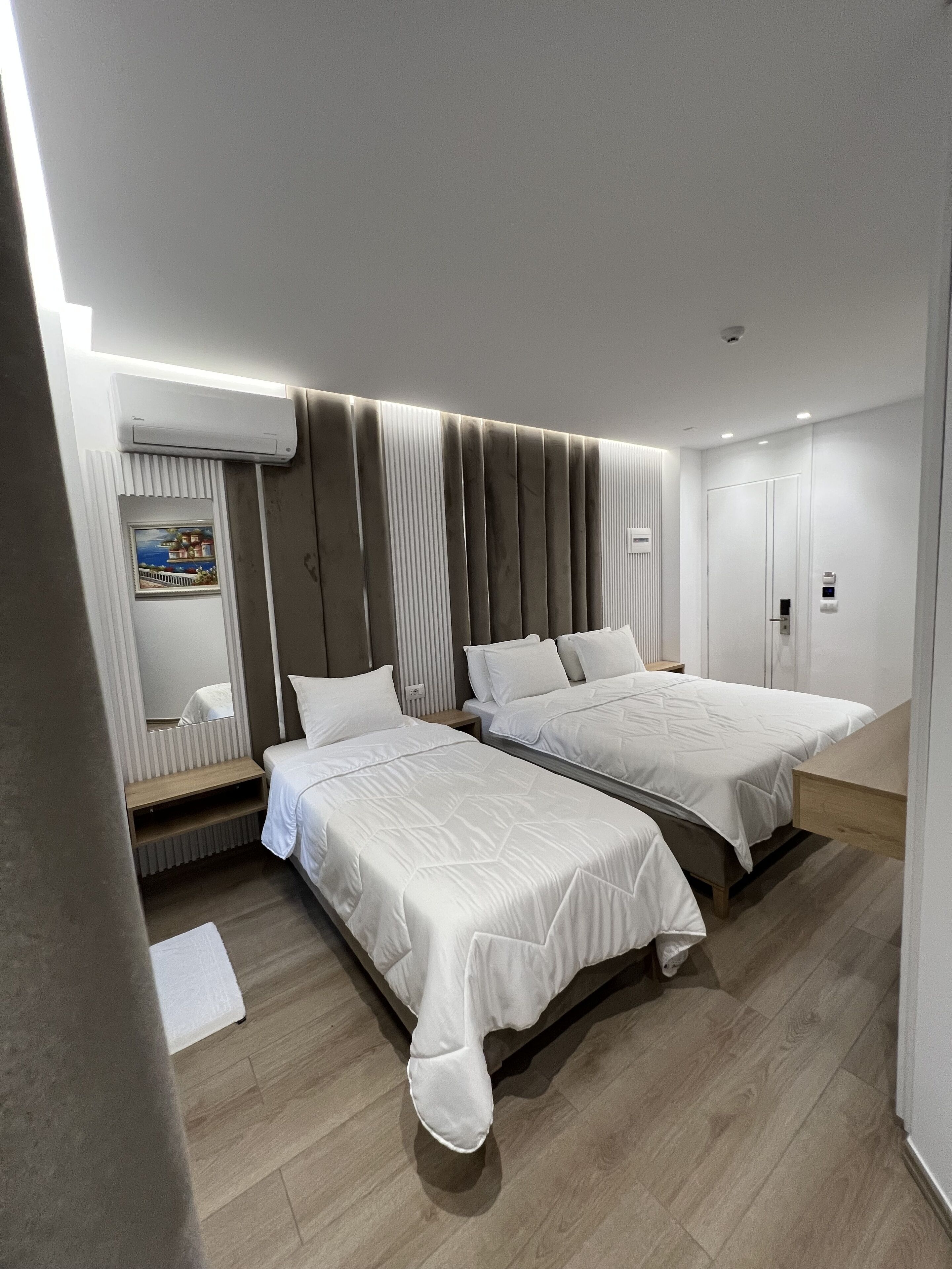 Habitació d'hotel moderna amb dos llits, un tocador integrat i una finestra amb vista a un edifici.