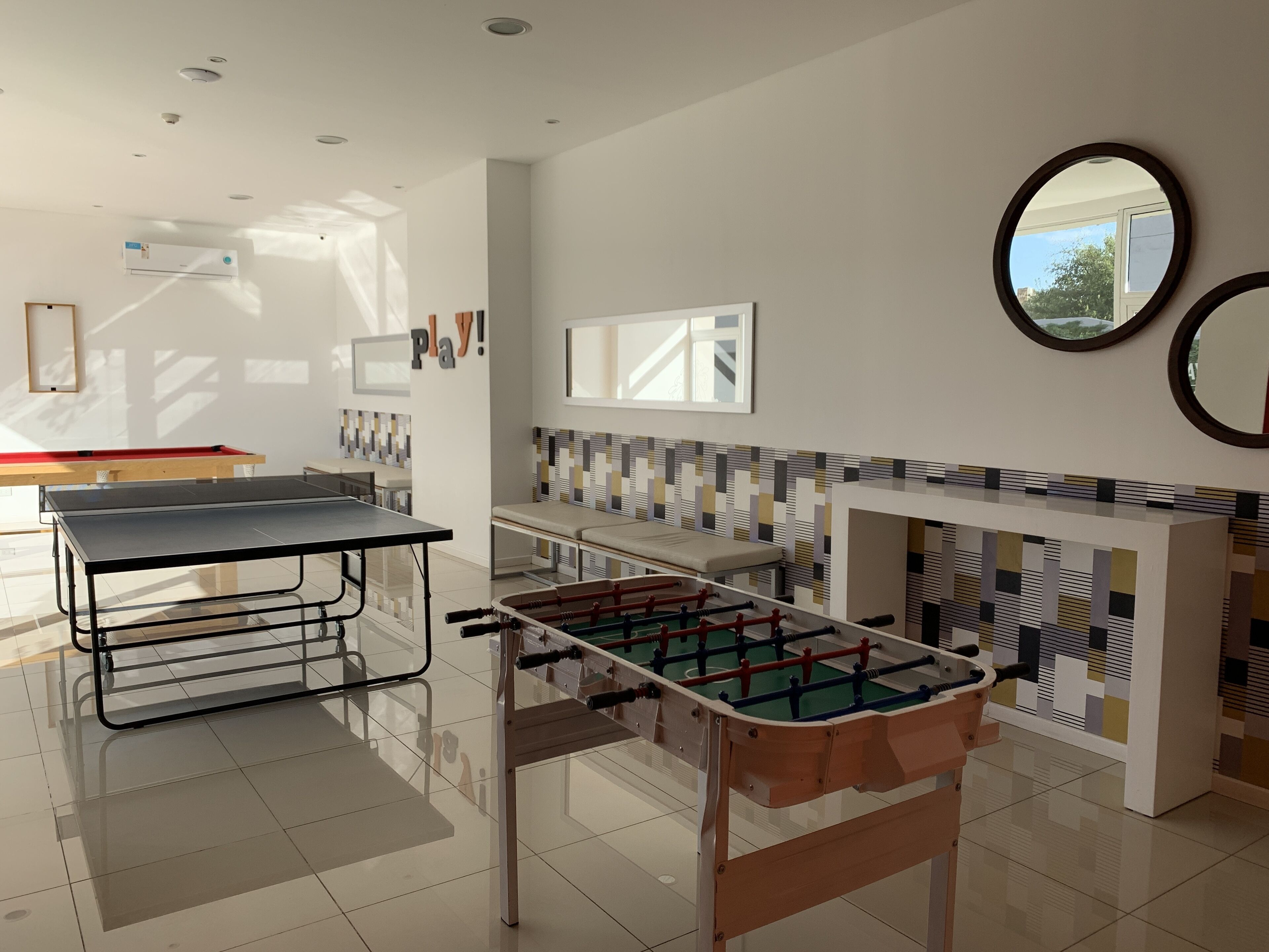 A modern indoor recreational area with a foosball table, ping pong table, and a billiards table.