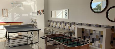 A modern indoor recreational area with a foosball table, ping pong table, and a billiards table.
