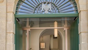 Entrada de un hotel con una puerta verde, una escalera y un arco metálico decorativo en la parte superior.