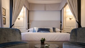 Habitación de hotel con una cama grande, dos sillones, una mesa de centro de cristal con un florero y dos lámparas de noche.