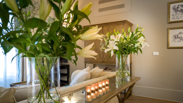 Una habitación con una mesa de vidrio que sostiene velas y jarrones con flores.