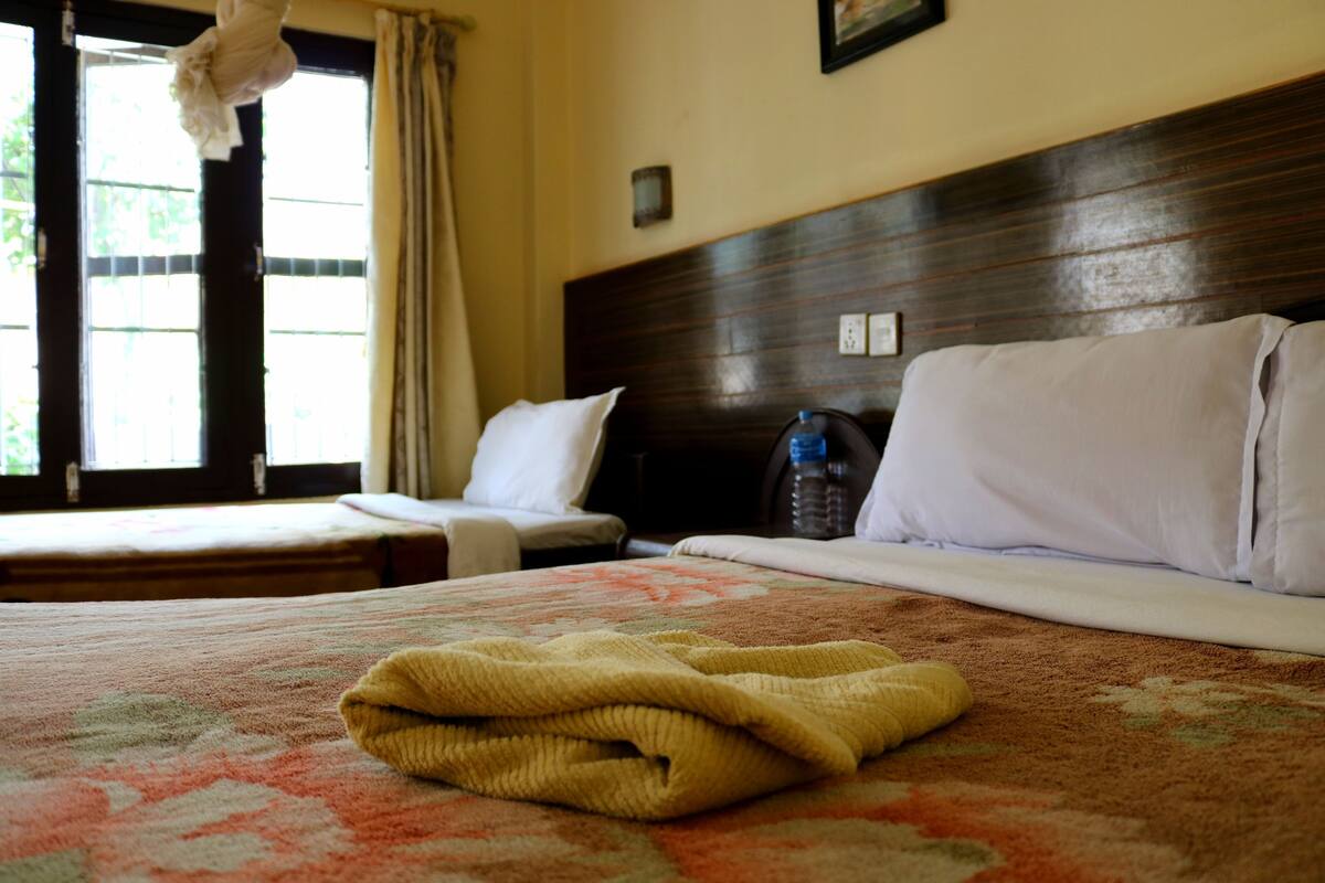 A hotel room with two beds, a wooden headboard, a window with curtains, and a water bottle on the nightstand.