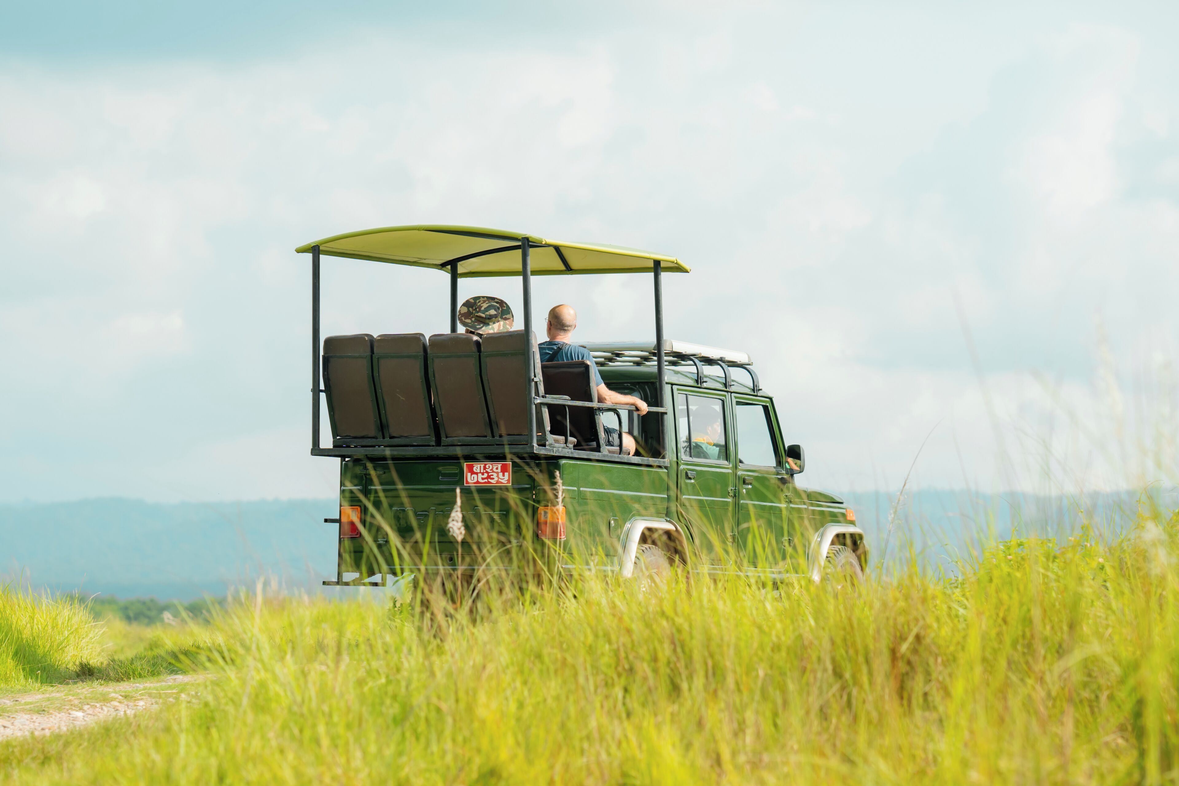 A green vehicle with a canopy and luggage, parked in a grassy area with a clear sky.