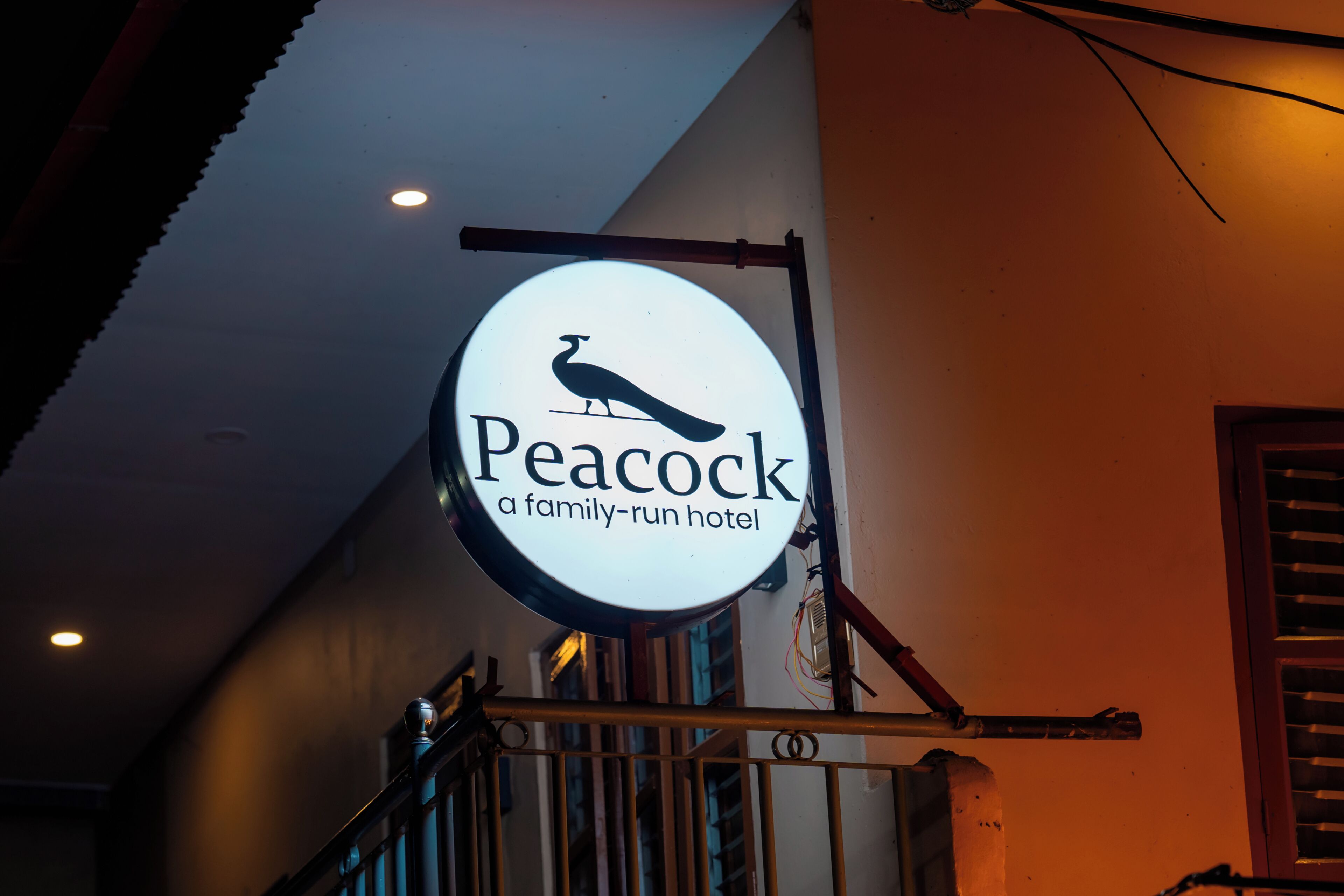 A circular sign with a peacock and the text 'Peacock a family-run hotel' against a building's interior.