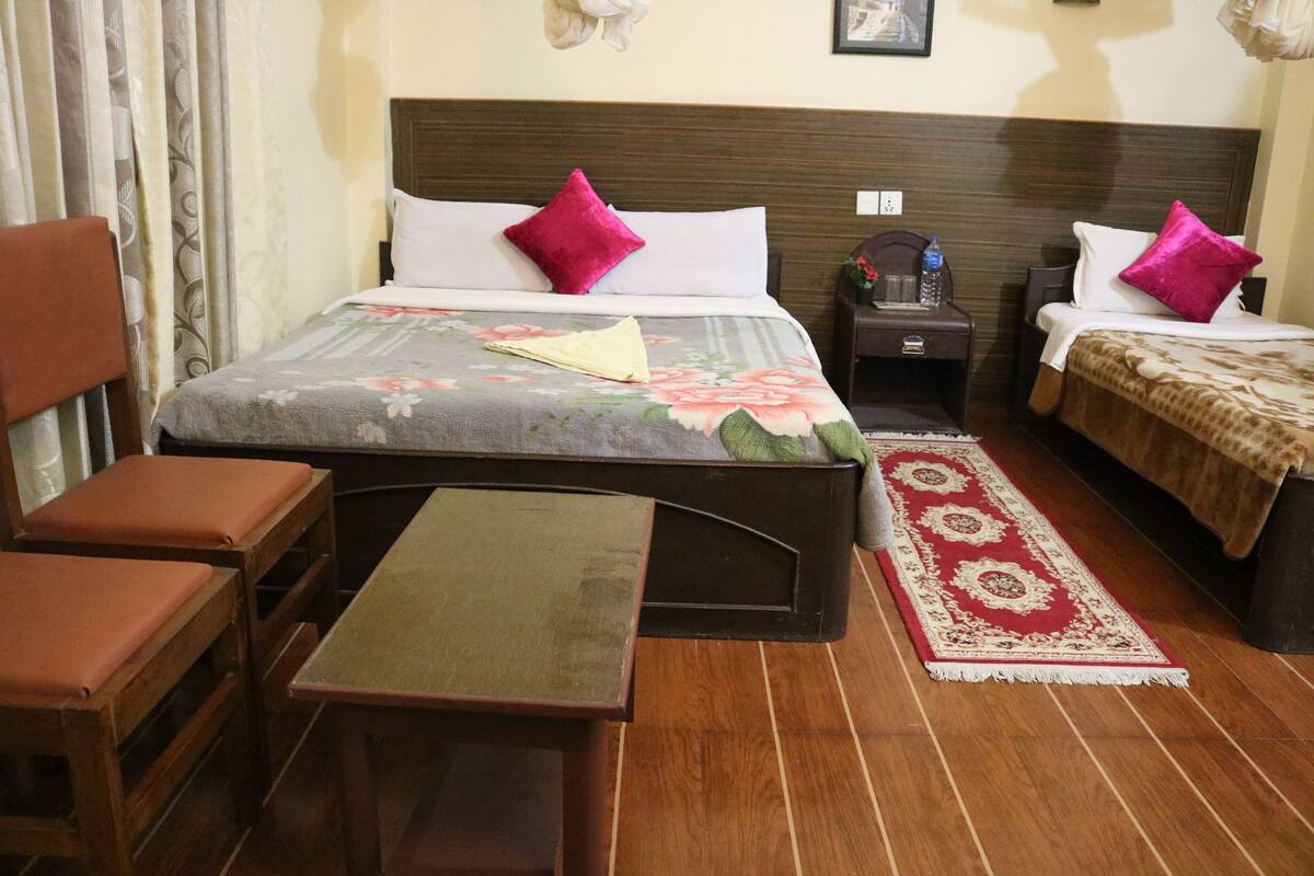 A hotel room with a bed, a desk, a chair, a nightstand, and a bedside table.