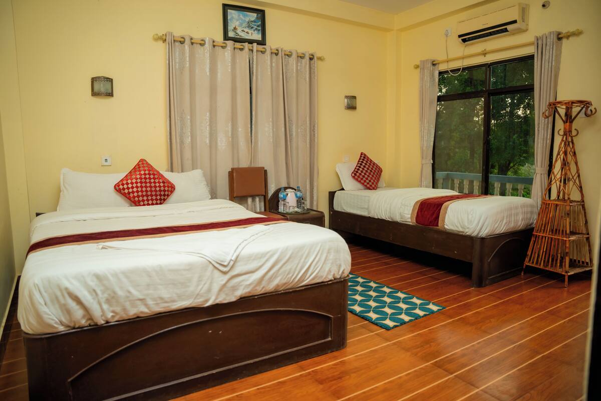 A room with two beds, a window with curtains, a wooden floor, and a small table with a chair.