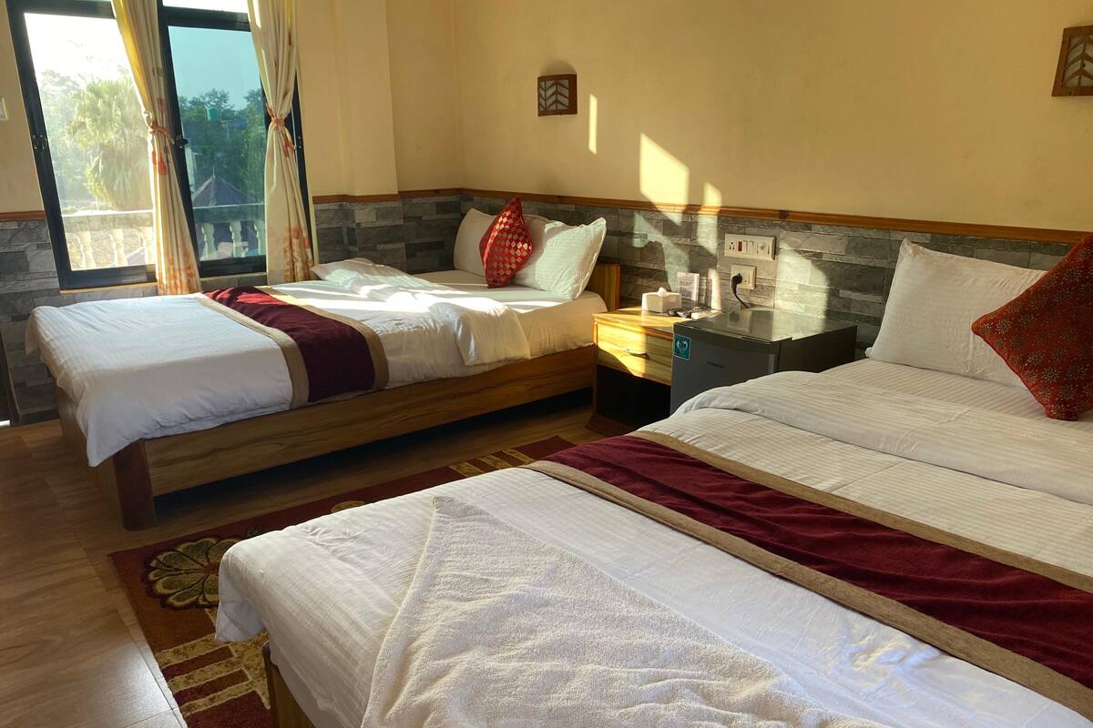 A hotel room with two beds, a nightstand, a heater, and a view of the outdoors.