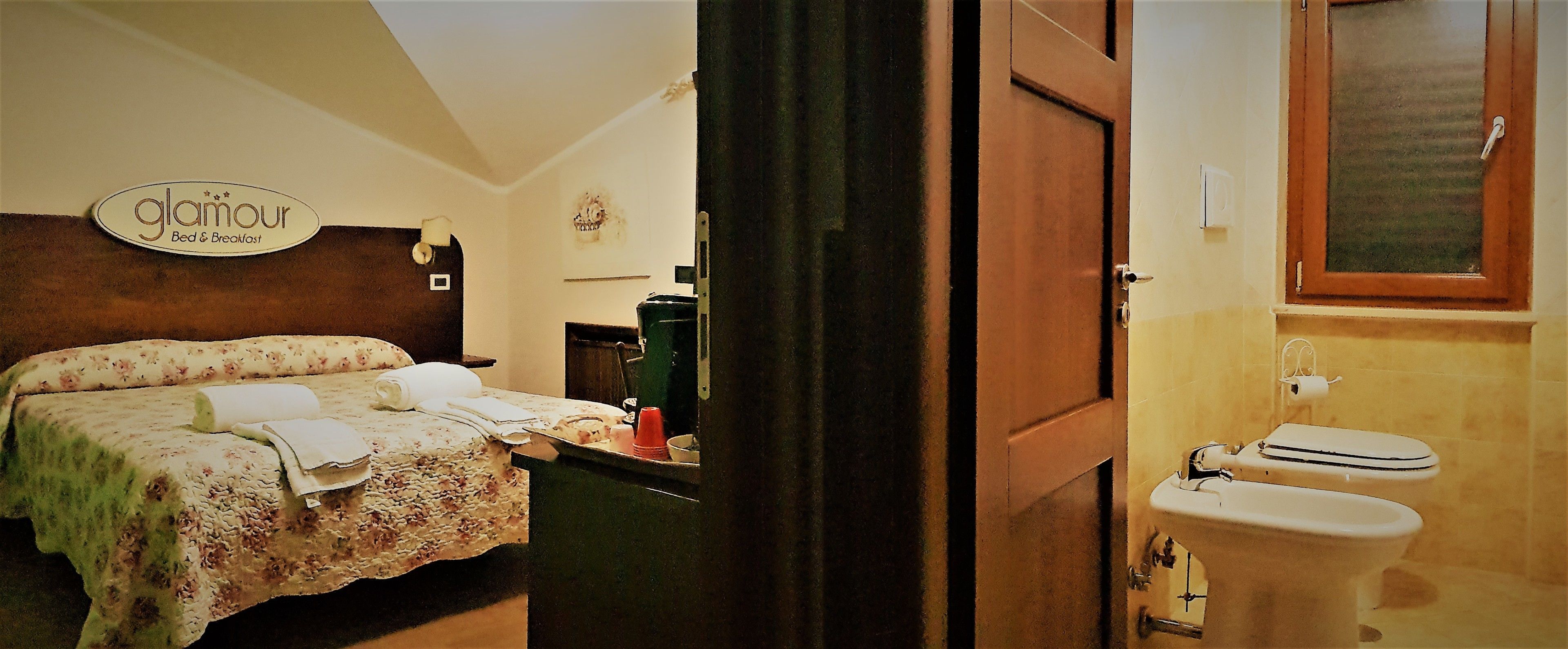A bedroom with a bed, a bedside table, a nightstand, a wall-mounted sign, and a bathroom with a toilet and sink.
