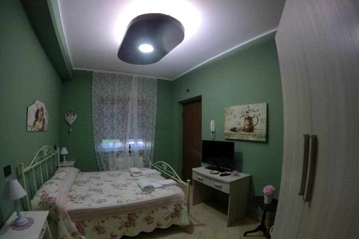Ein Schlafzimmer mit Bett, Nachttisch, Lampe, Fernseher und Schreibtisch.