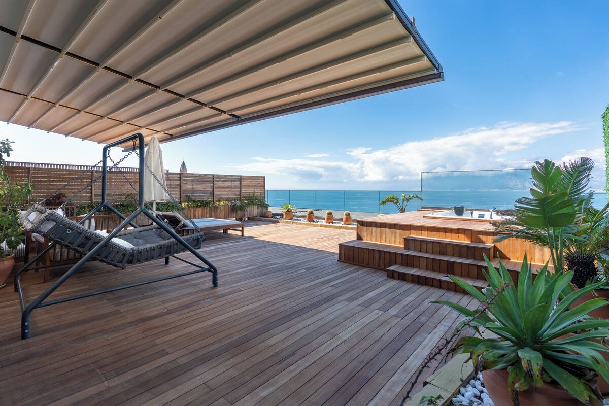 A wooden deck with a swing chair, a hot tub, and potted plants.
