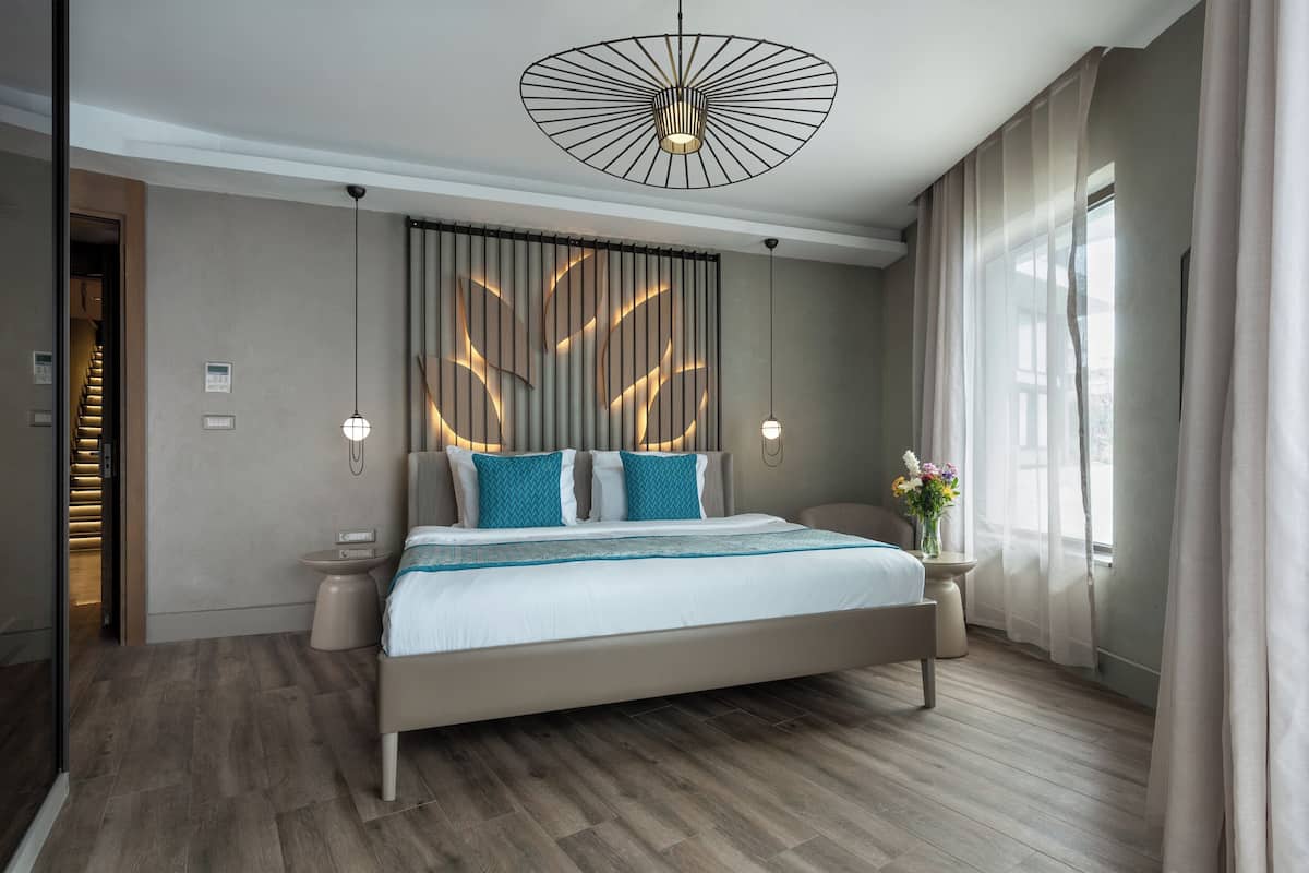 A modern bedroom with a large bed, two bedside tables, a wall-mounted light fixture, and a window with curtains.