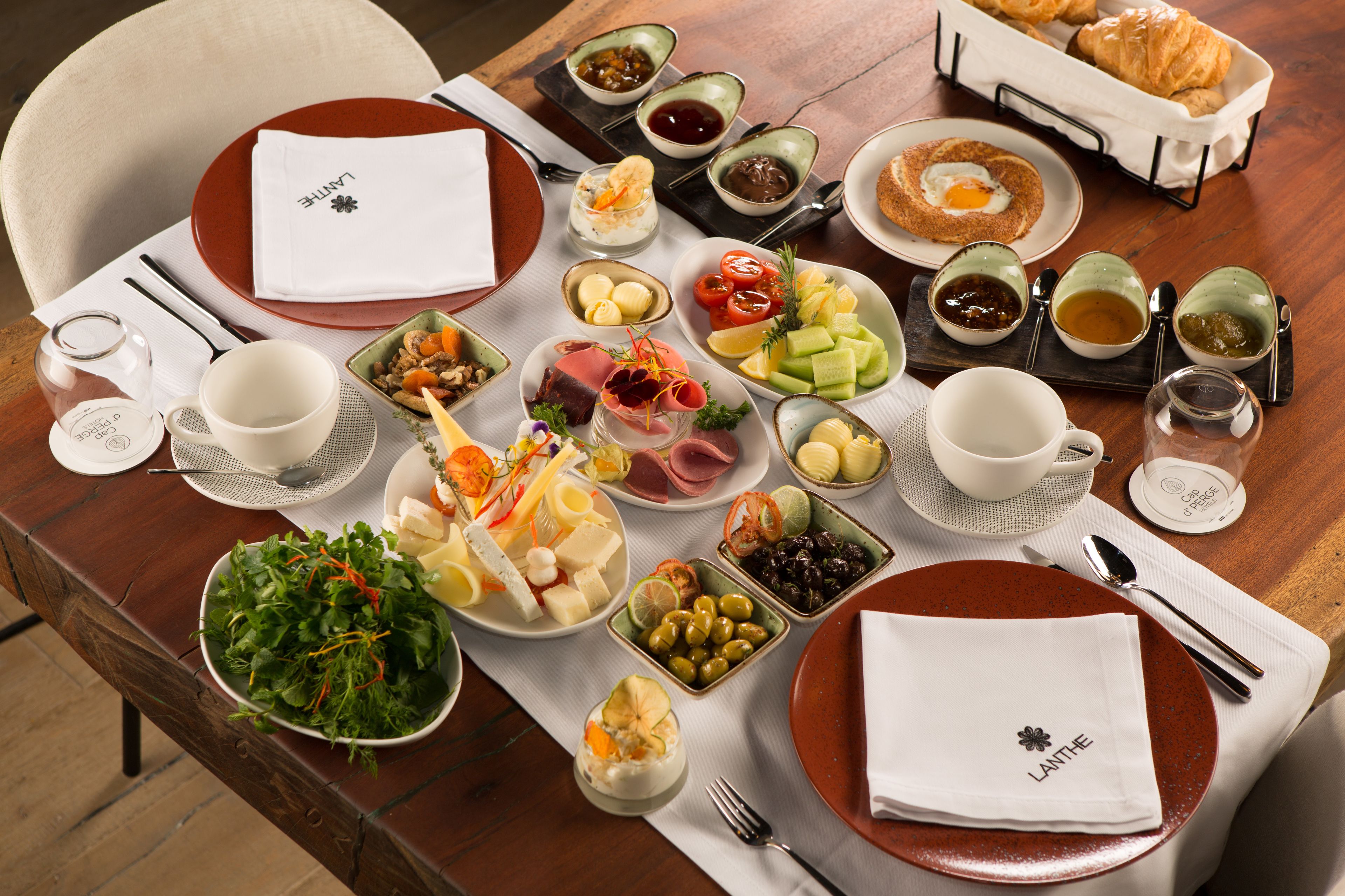 A well-set dining table with various dishes, including salads, meats, and pastries, arranged on a wooden table.