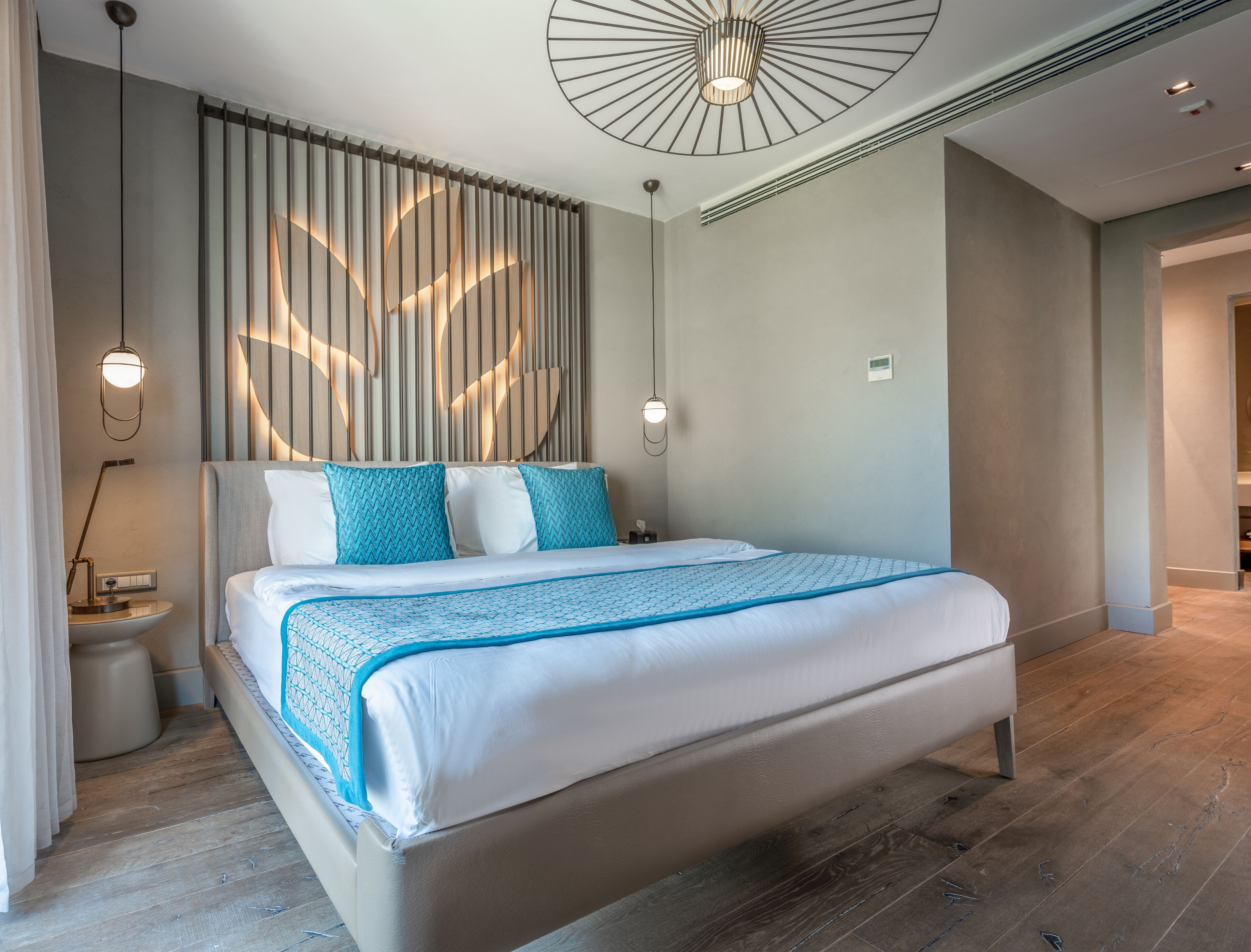 A modern hotel room with a large bed, a wall-mounted light fixture, and a ceiling fan.