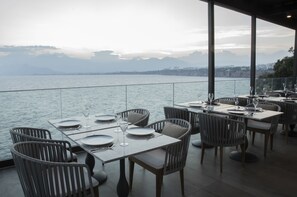 Un restaurante con mesas dispuestas para comer, con vista a un cuerpo de agua y montañas al fondo.