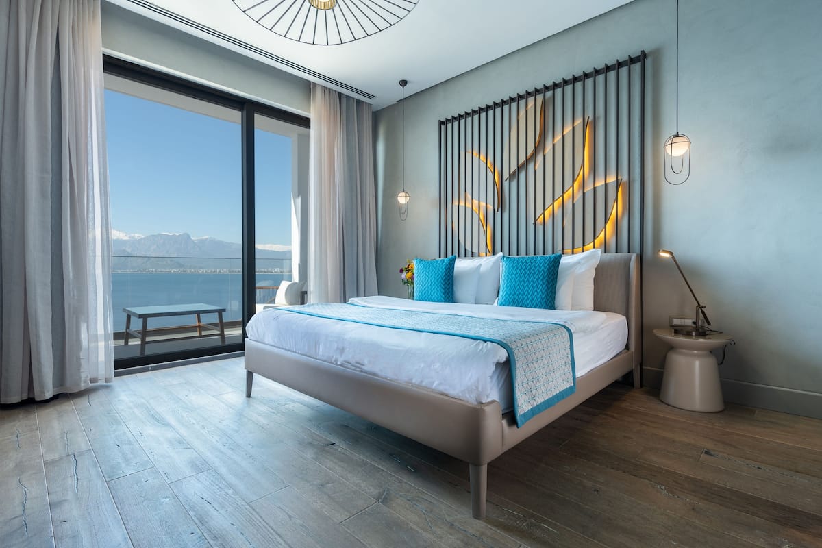 A modern hotel room with a large bed, a view of the mountains, and a balcony.