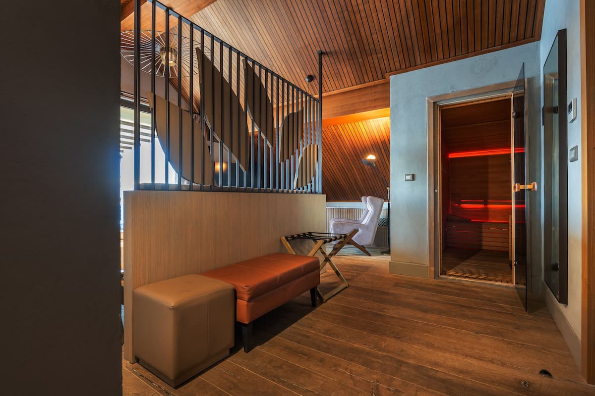 A modern interior with a wooden staircase, a bench, and a door leading to a red-lit room.
