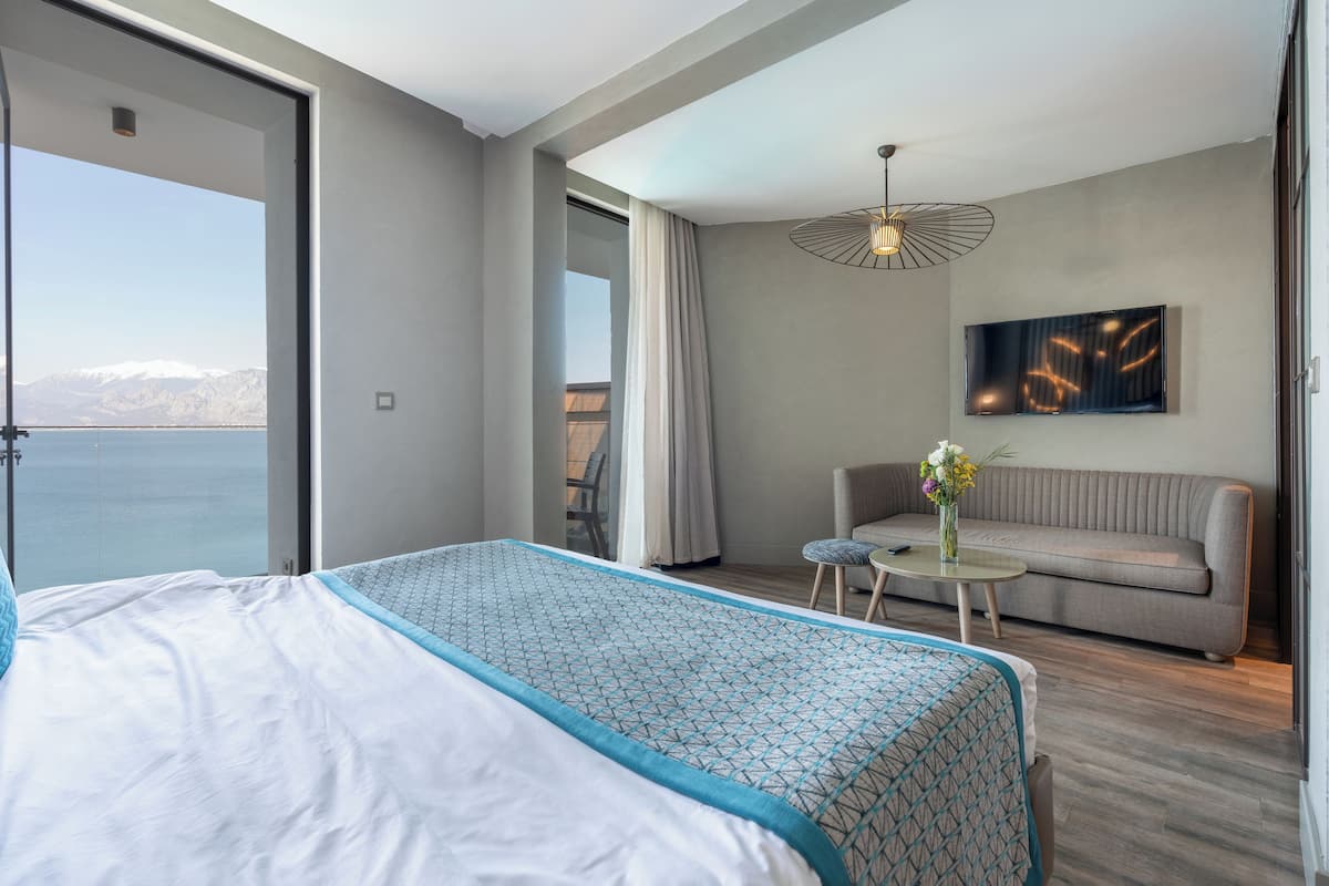 A modern hotel room with a large bed, a sofa, a small table with a vase, and a view of the mountains.