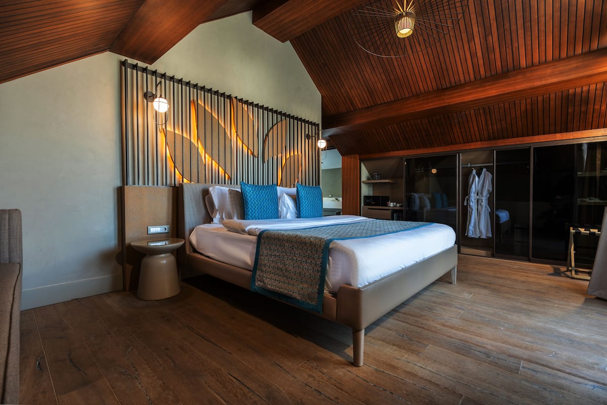 A modern bedroom with a large bed, wooden flooring, a built-in bench, a bedside table, and a wall-mounted light fixture.