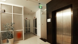 A modern elevator with a metallic finish, a glass door, and a red exit sign above.