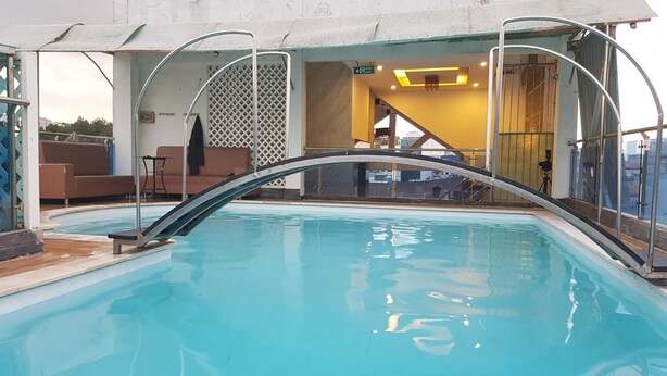 A pool with a curved glass barrier, a sofa, and a staircase leading to an upper deck.