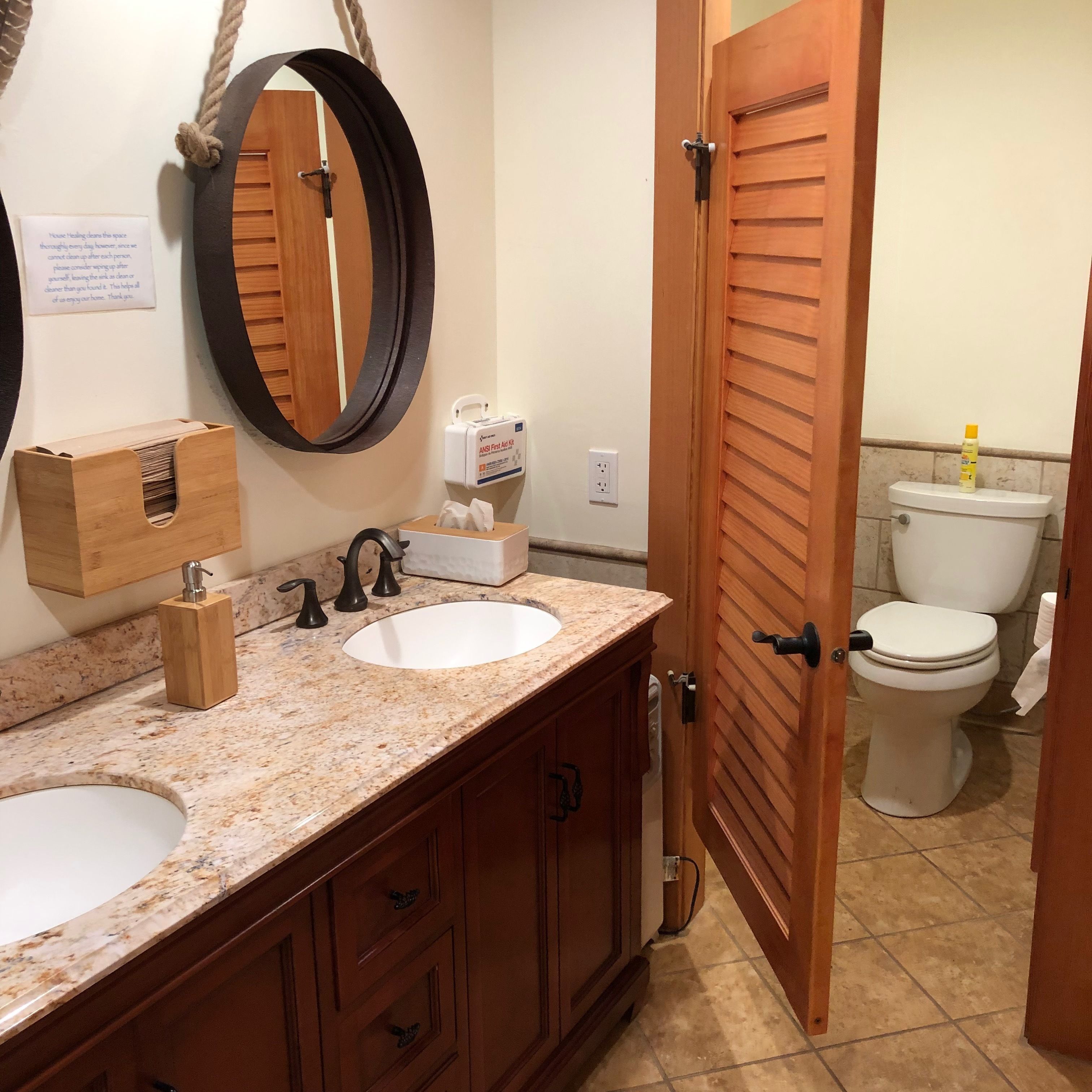 A bathroom with two sinks, a mirror, a wooden cabinet, a toilet, and a door.