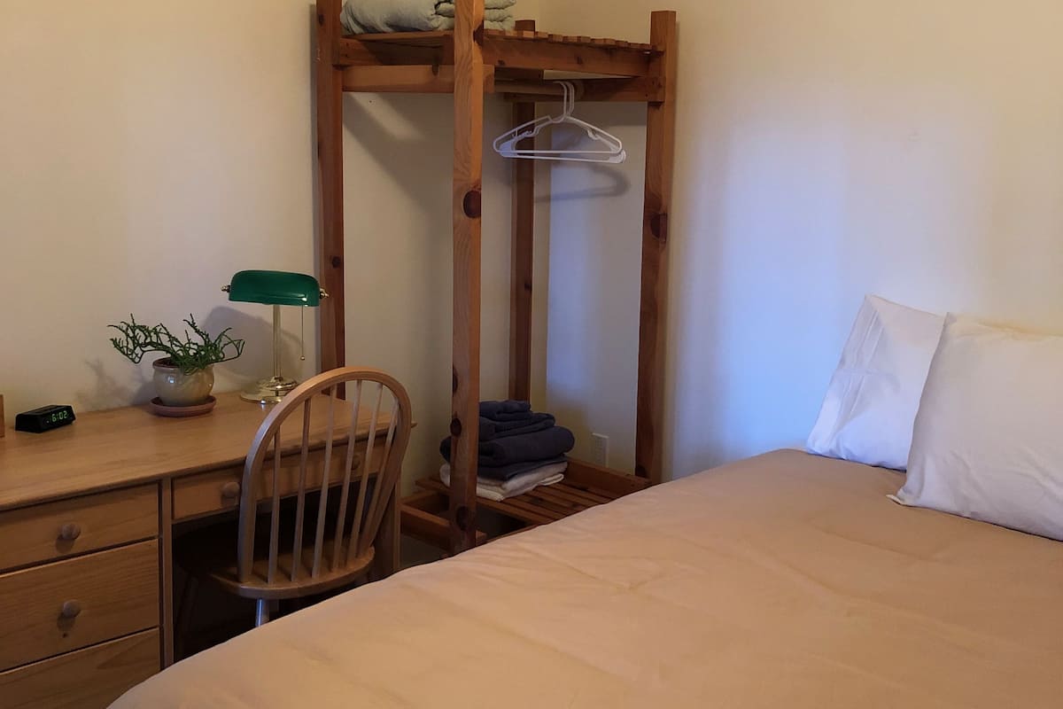 Ein Schlafzimmer mit Etagenbett, Schreibtisch mit Stuhl, Nachttisch, Pendelleuchte und einer Topfpflanze.