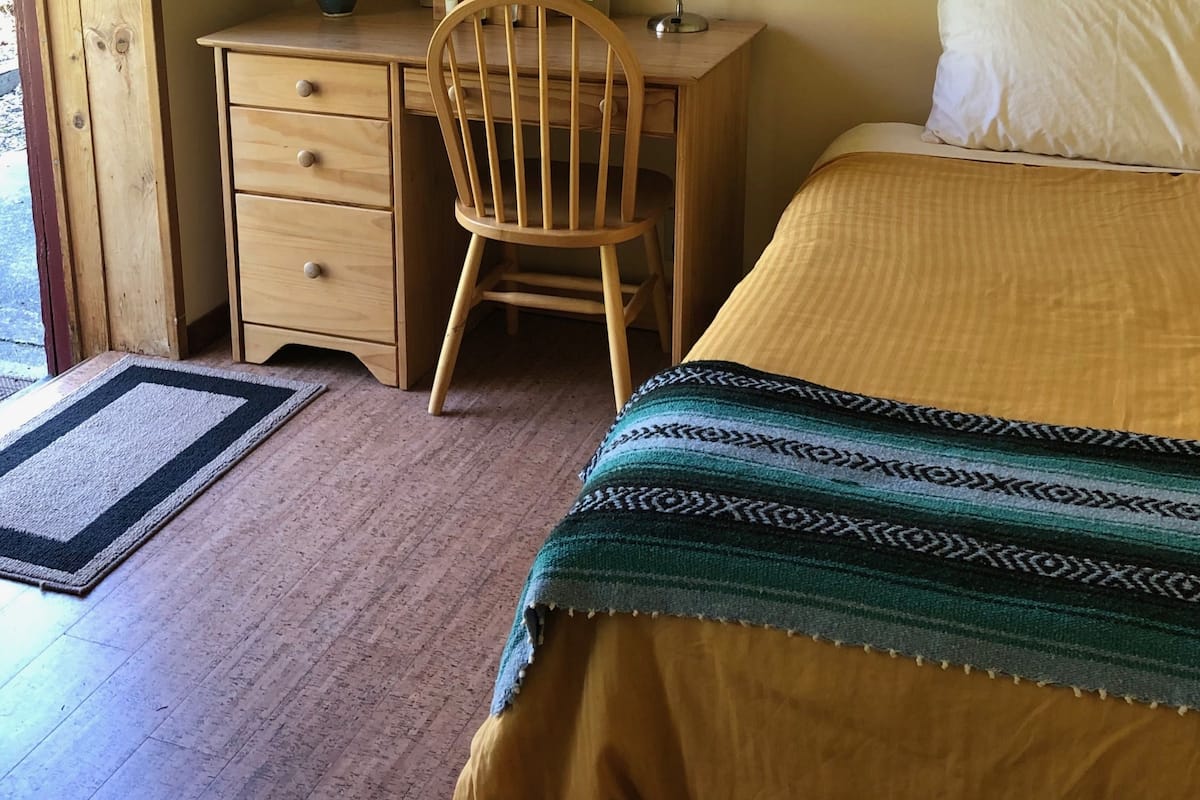 Ein Schlafzimmer mit einem Holztisch, einem Stuhl, einem Bett mit gemustertem Überwurf und einer Nachttischlampe.