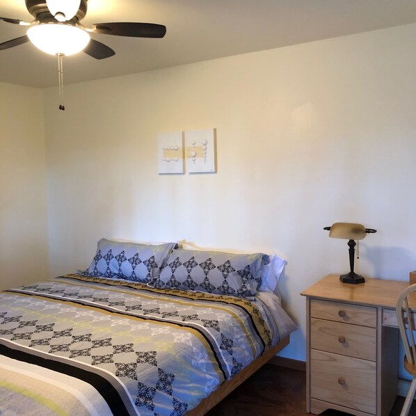 Ein Schlafzimmer mit Bett, Nachttisch, Lampe und Deckenventilator.