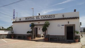 A building labeled "Hostal El Canario" with a tiled roof, a signboard, and potted plants in front. - Hostal El Canario (Conil de la Frontera)