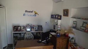 A reception desk with a wooden finish, a wall-mounted sign reading "Hostal El Canario", and various items including a computer, a chair, and decorative objects. - Hostal El Canario (Conil de la Frontera)