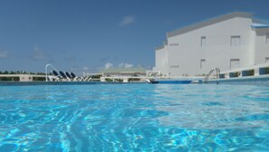 En swimmingpool med krystalklart blå vand, liggestole og en hvid bygning i baggrunden.