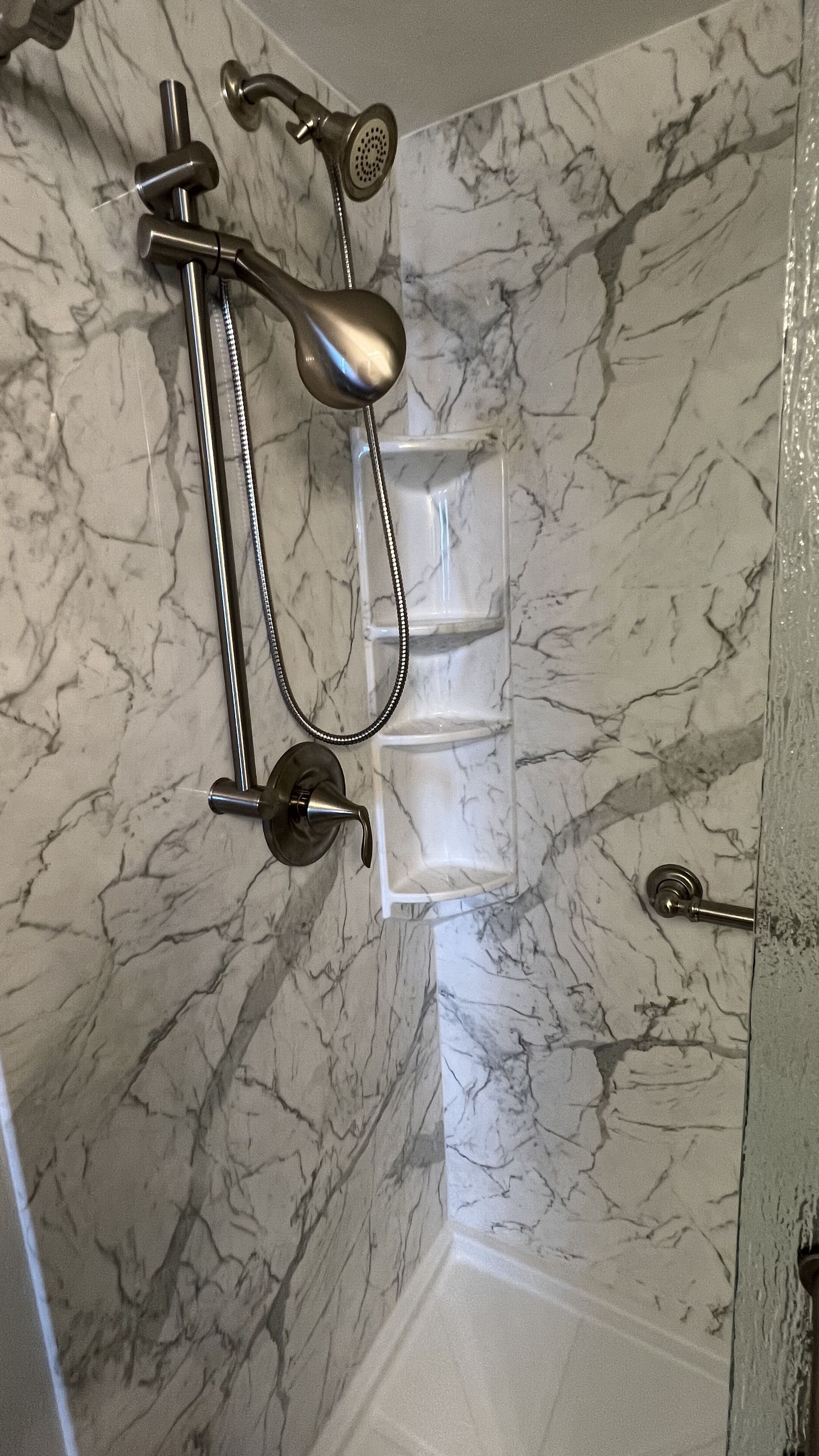 Un baño con ducha, bañera con cerramiento de vidrio y pared de mármol.
