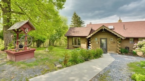 A log cabin with a gravel driveway and a garden area with a birdhouse and a decorative windmill.