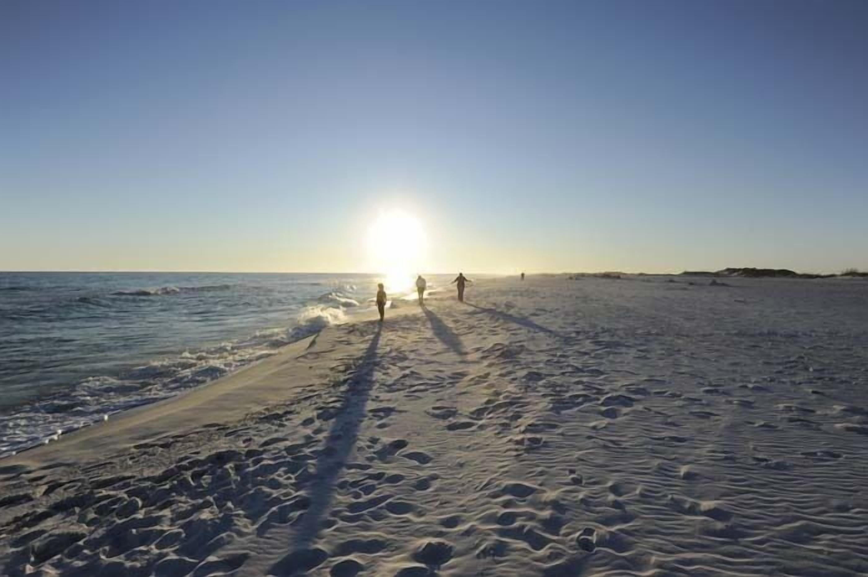 Een strand met voetafdrukken die naar het water leiden, een heldere lucht en een lage zonsondergang.