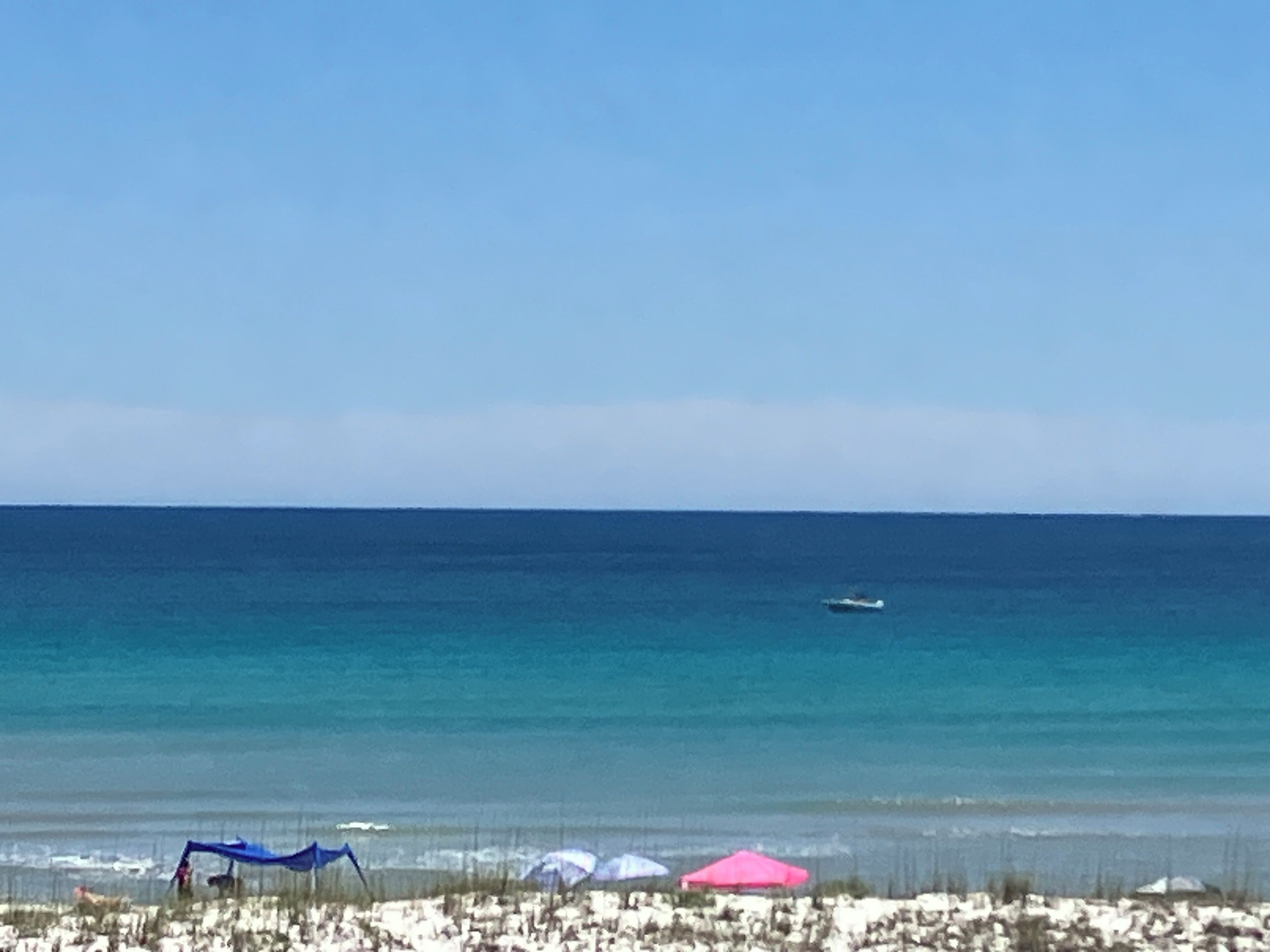 Une plage avec un ciel dégagé, un bateau sur l’eau et des parasols de plage.